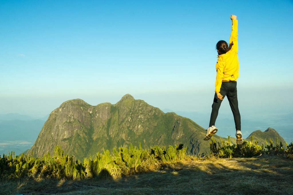 dağ manzarası önünde zıplayan insan, sarı kazak